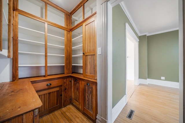 interior space with light wood-style flooring, baseboards, visible vents, and ornamental molding