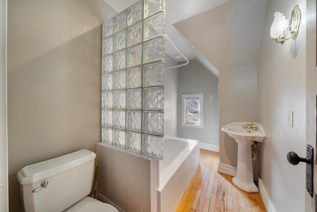 bathroom with a bath, baseboards, lofted ceiling, wood-type flooring, and toilet