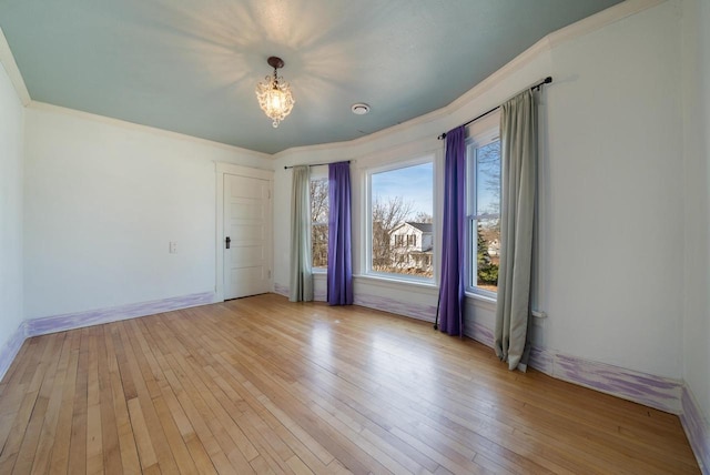 unfurnished room with light wood-type flooring, baseboards, ornamental molding, and a chandelier