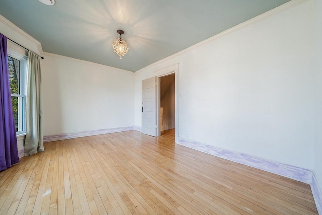 spare room featuring a chandelier, baseboards, ornamental molding, and light wood finished floors