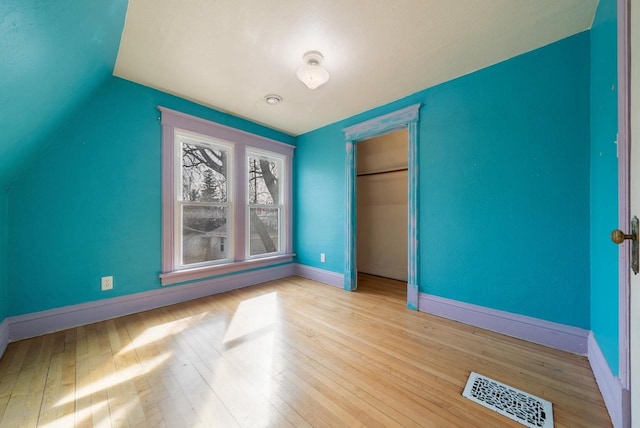 unfurnished bedroom with visible vents, hardwood / wood-style floors, a closet, baseboards, and vaulted ceiling