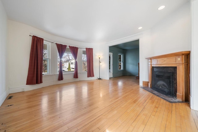 unfurnished living room featuring recessed lighting, a fireplace with raised hearth, baseboards, and light wood-style floors