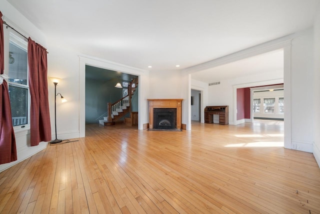 unfurnished living room featuring light wood finished floors, visible vents, baseboards, stairway, and a fireplace with flush hearth