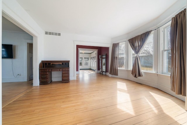 unfurnished living room with light wood-type flooring, visible vents, and baseboards