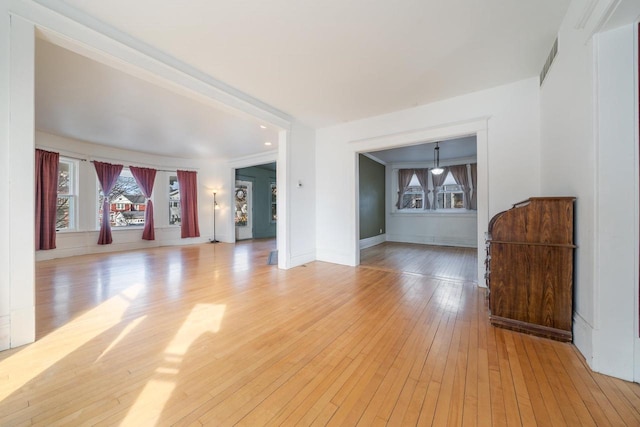 unfurnished living room featuring visible vents, light wood-style flooring, and baseboards