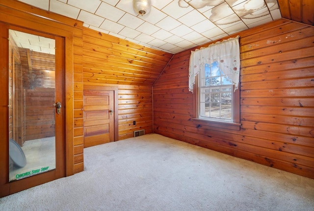 additional living space featuring visible vents, wood walls, lofted ceiling, and carpet floors