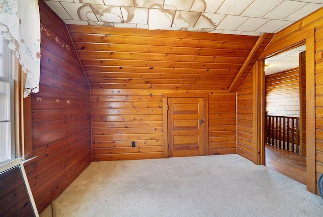 carpeted spare room with lofted ceiling and wood walls