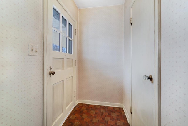 doorway to outside with wallpapered walls, brick floor, and baseboards