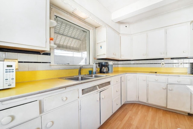 kitchen with tasteful backsplash, light countertops, light wood-style flooring, white cabinetry, and a sink