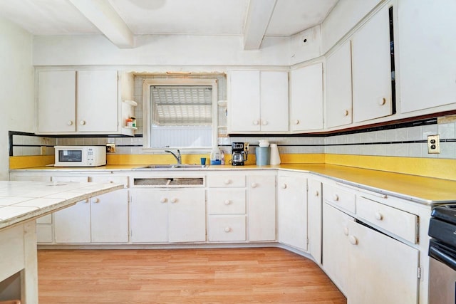 kitchen featuring light wood finished floors, beam ceiling, white microwave, and white cabinetry