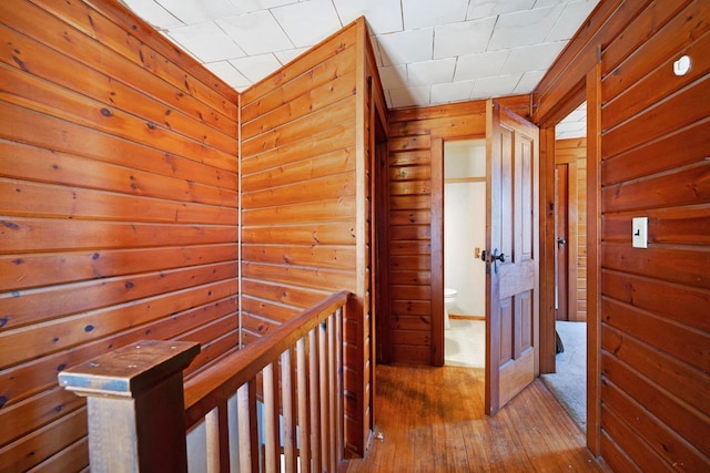 hall with wood-type flooring, wooden walls, and an upstairs landing