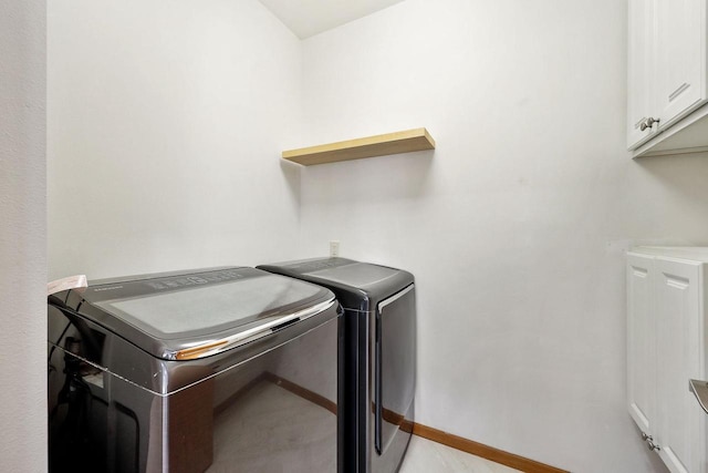 clothes washing area featuring baseboards, cabinet space, and washing machine and dryer