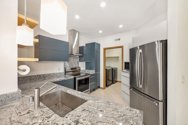 kitchen with wall chimney range hood, appliances with stainless steel finishes, washer and dryer, modern cabinets, and a sink