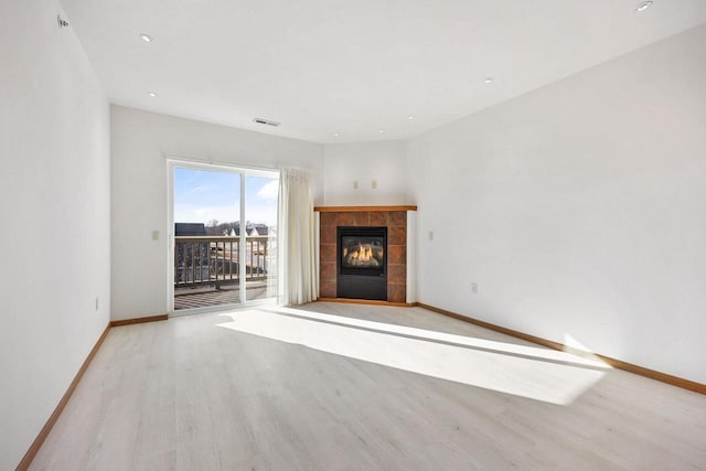 unfurnished living room featuring a tiled fireplace, visible vents, baseboards, and wood finished floors