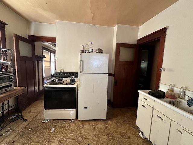 kitchen with freestanding refrigerator, a sink, light countertops, white cabinets, and range with electric stovetop