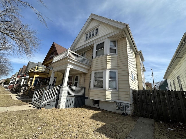 view of side of property with a balcony, fence, and covered porch