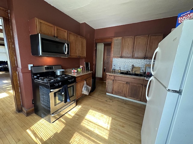 kitchen featuring light wood finished floors, brown cabinets, appliances with stainless steel finishes, and a sink