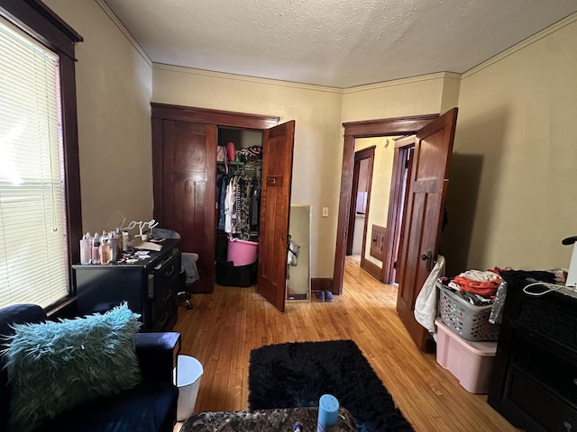 bedroom with baseboards, ornamental molding, a closet, a textured ceiling, and light wood-type flooring