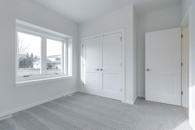 unfurnished bedroom featuring a closet, visible vents, light colored carpet, and baseboards