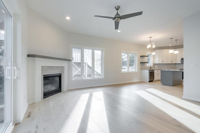 unfurnished living room with visible vents, recessed lighting, a glass covered fireplace, ceiling fan with notable chandelier, and light wood-type flooring