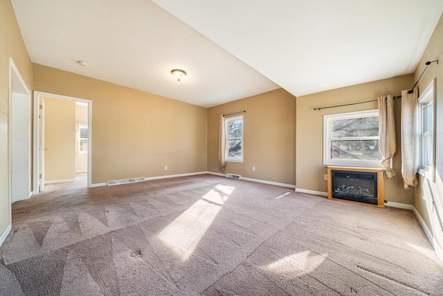 empty room featuring visible vents, carpet flooring, baseboards, and a glass covered fireplace