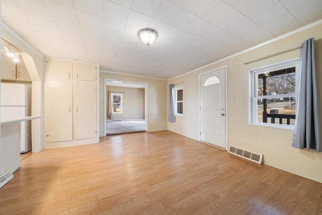 interior space featuring light wood finished floors, visible vents, and crown molding