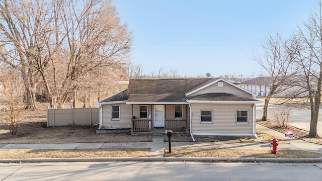 view of front facade with roof with shingles, covered porch, and fence