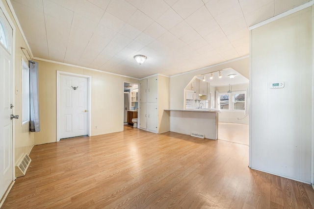 unfurnished living room featuring a sink, light wood-type flooring, visible vents, and ornamental molding