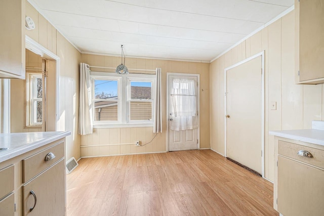 unfurnished dining area featuring light wood-style floors, visible vents, and ornamental molding