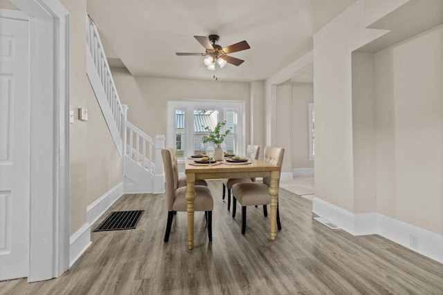 dining area with ceiling fan, visible vents, wood finished floors, and stairway