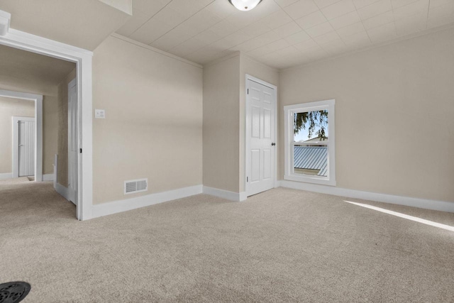 carpeted empty room with visible vents, baseboards, and ornamental molding