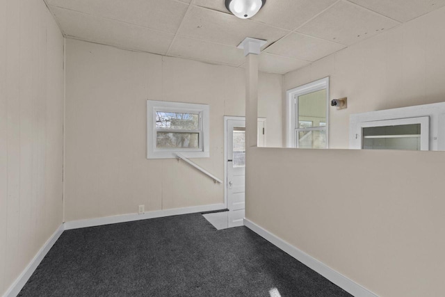 carpeted spare room featuring a paneled ceiling, plenty of natural light, and baseboards