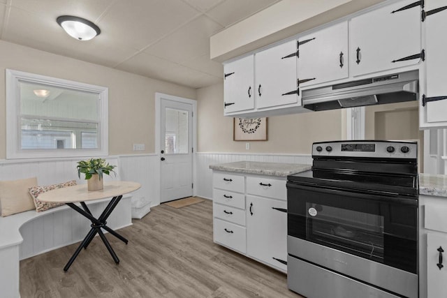 kitchen with under cabinet range hood, stainless steel electric stove, light countertops, and a wainscoted wall