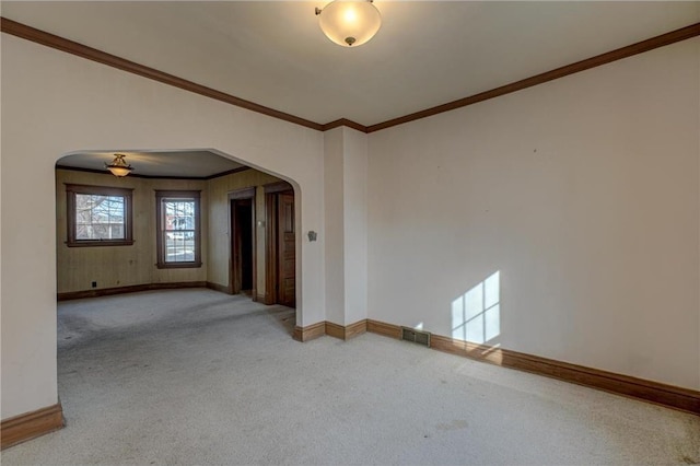 carpeted spare room with baseboards, arched walkways, and ornamental molding