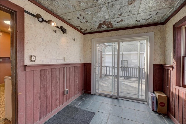 doorway to outside with wallpapered walls, ornamental molding, an ornate ceiling, and wainscoting