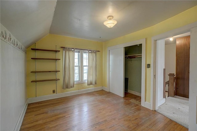 unfurnished bedroom with hardwood / wood-style flooring, baseboards, a closet, and vaulted ceiling