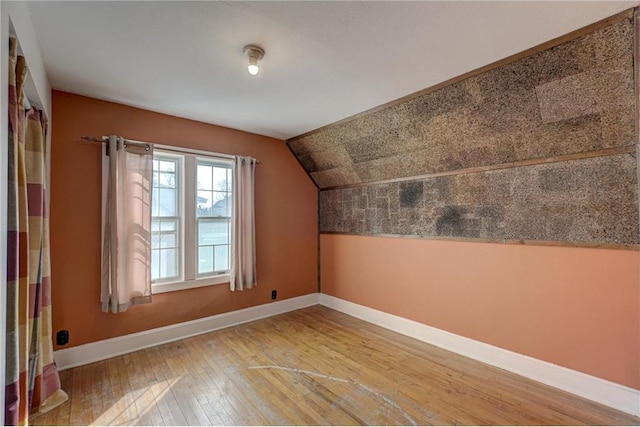 additional living space with light wood-type flooring, baseboards, and vaulted ceiling