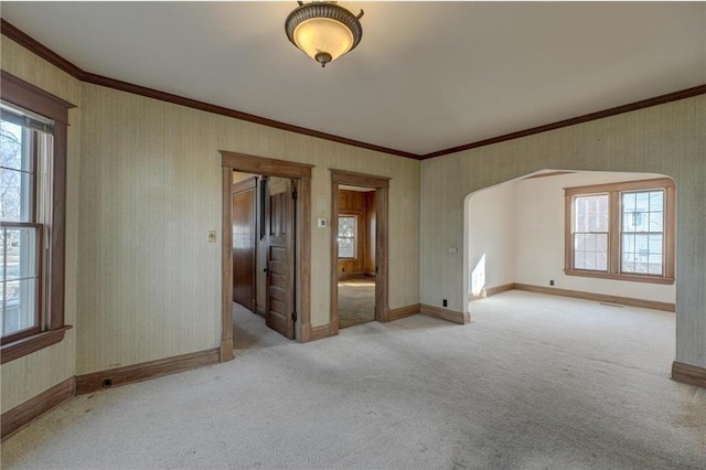 empty room with arched walkways, light carpet, wallpapered walls, and ornamental molding