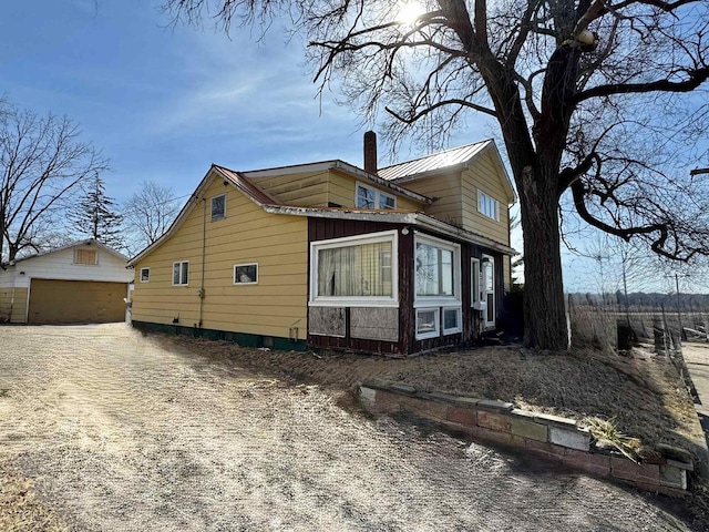 view of home's exterior featuring driveway, a chimney, an outdoor structure, and metal roof