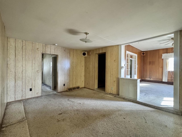 carpeted empty room featuring visible vents, baseboards, ceiling fan, and wood walls