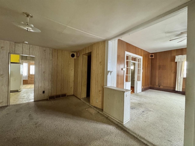 carpeted spare room featuring visible vents, wood walls, and ceiling fan