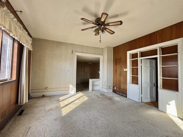 unfurnished room with wooden walls, visible vents, a ceiling fan, and carpet