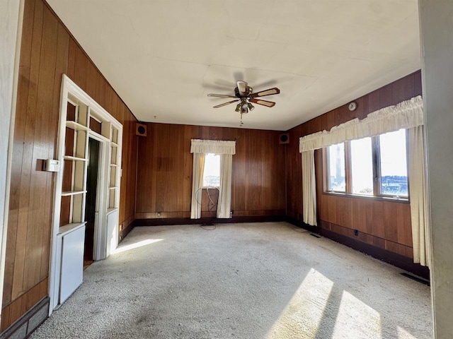 unfurnished room featuring plenty of natural light, light colored carpet, wooden walls, and ceiling fan