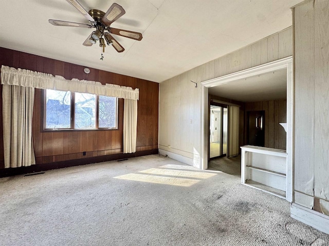 carpeted empty room featuring visible vents, wood walls, and ceiling fan