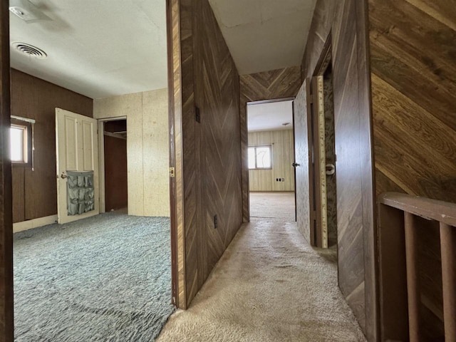 hallway with visible vents, carpet, and wood walls