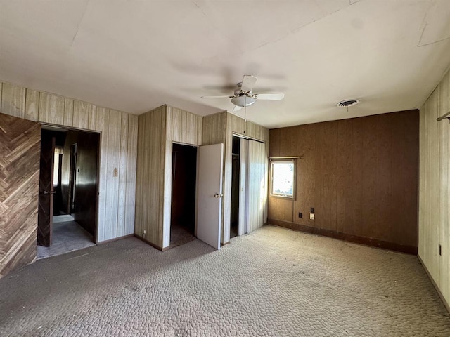 unfurnished bedroom with visible vents, baseboards, ceiling fan, wood walls, and light carpet