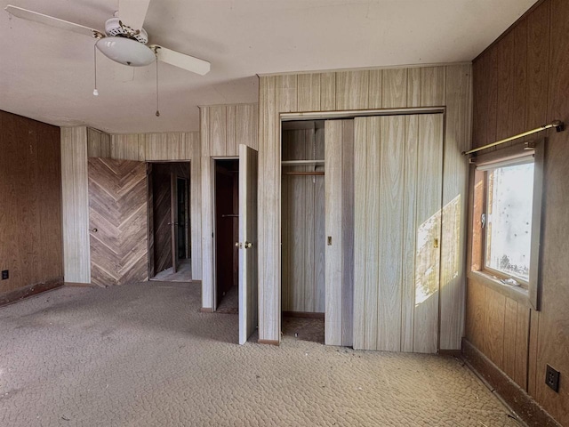 unfurnished bedroom featuring ceiling fan, carpet floors, two closets, and wood walls