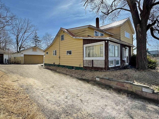 view of home's exterior featuring an outbuilding, driveway, a chimney, a detached garage, and metal roof