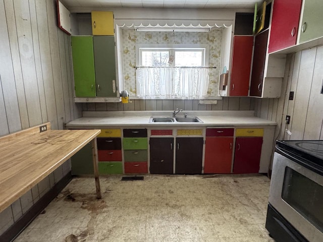 kitchen featuring a sink, wood walls, light countertops, stainless steel electric range oven, and light floors