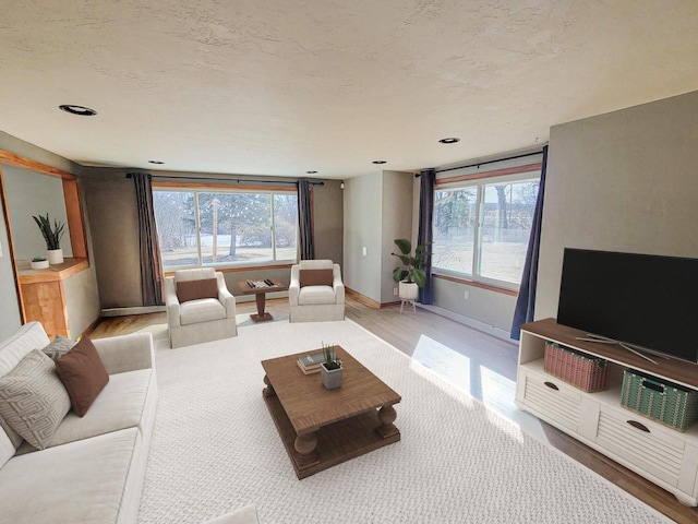 living room featuring a wealth of natural light, light wood-style flooring, a textured ceiling, and baseboards